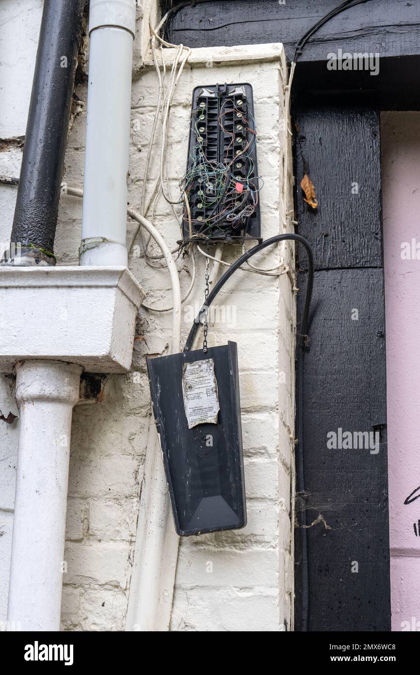 Broken telephone junction box hung on a wall with many wires loose from