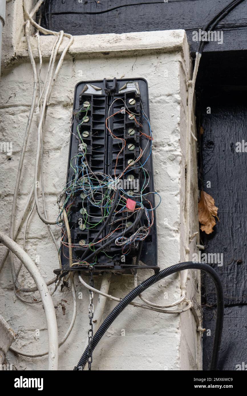 Broken telephone junction box hung on a wall with many wires loose from