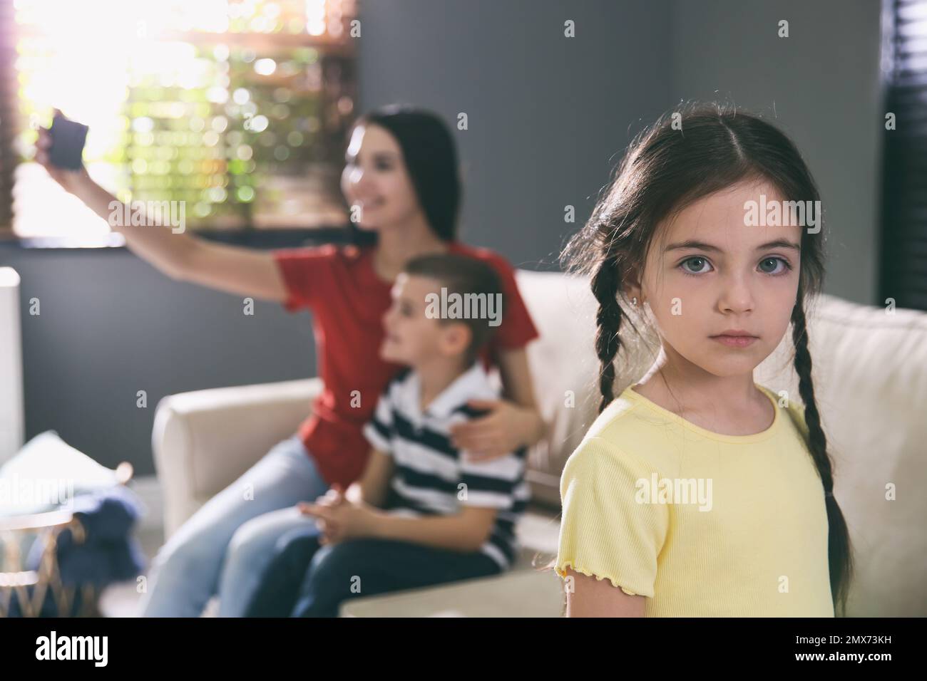 Unhappy little girl feeling jealous while mother taking selfie with her