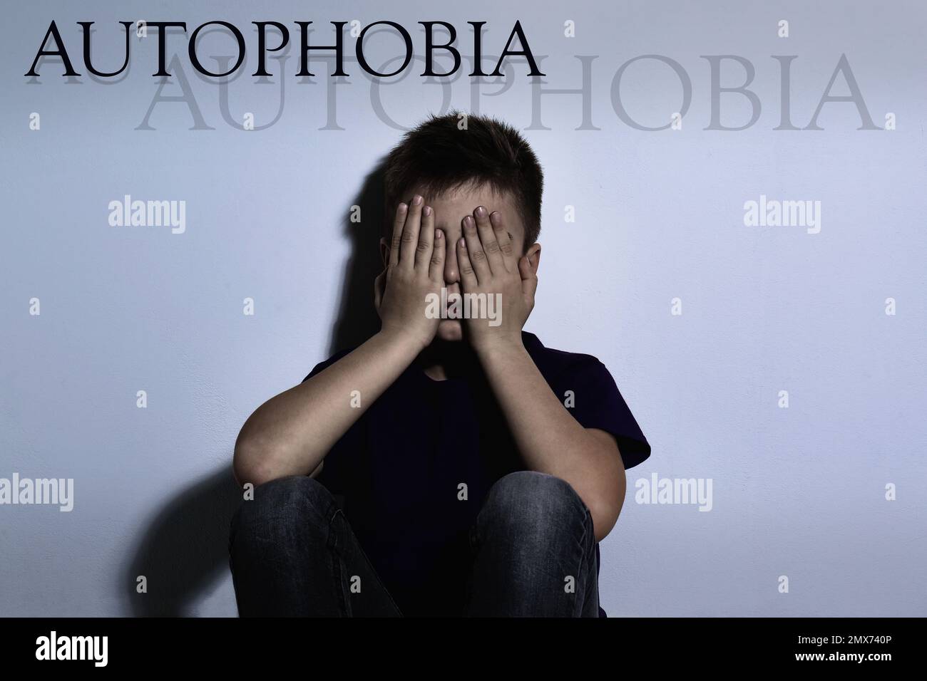 Upset boy closing eyes near white wall. Autophobia fear of isolation
