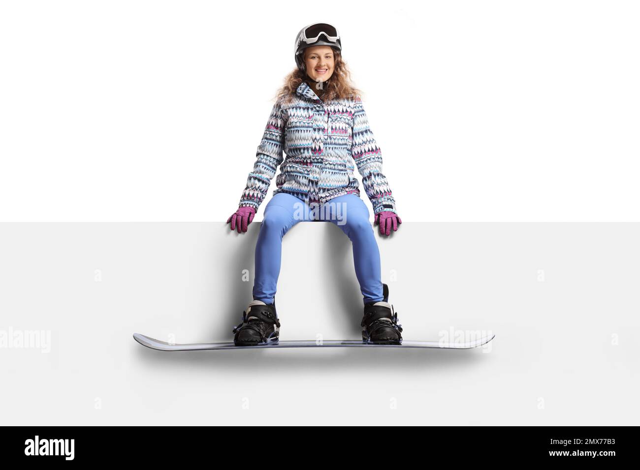 Young female snowboarder sitting on a blank panel isolated on white background Stock Photo