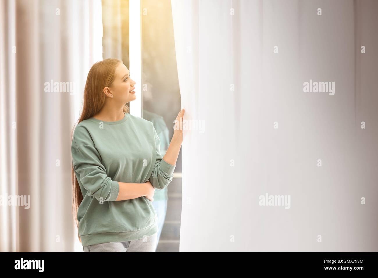 Beautiful young woman looking out of window at home Stock Photo - Alamy