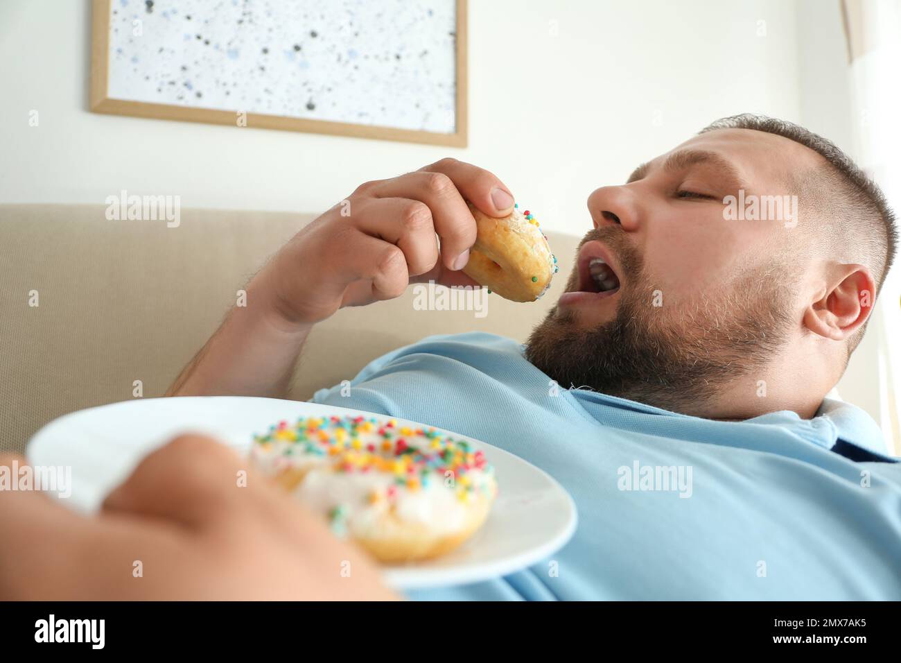 Lazy overweight man eating donuts at home, closeup Stock Photo