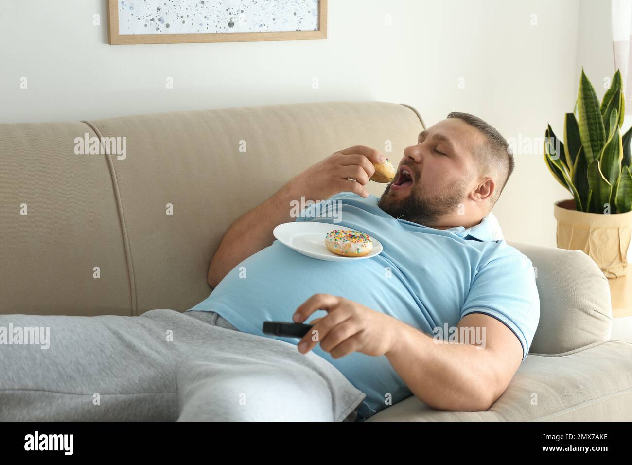 Lazy overweight man with donuts watching TV on sofa at home Stock Photo