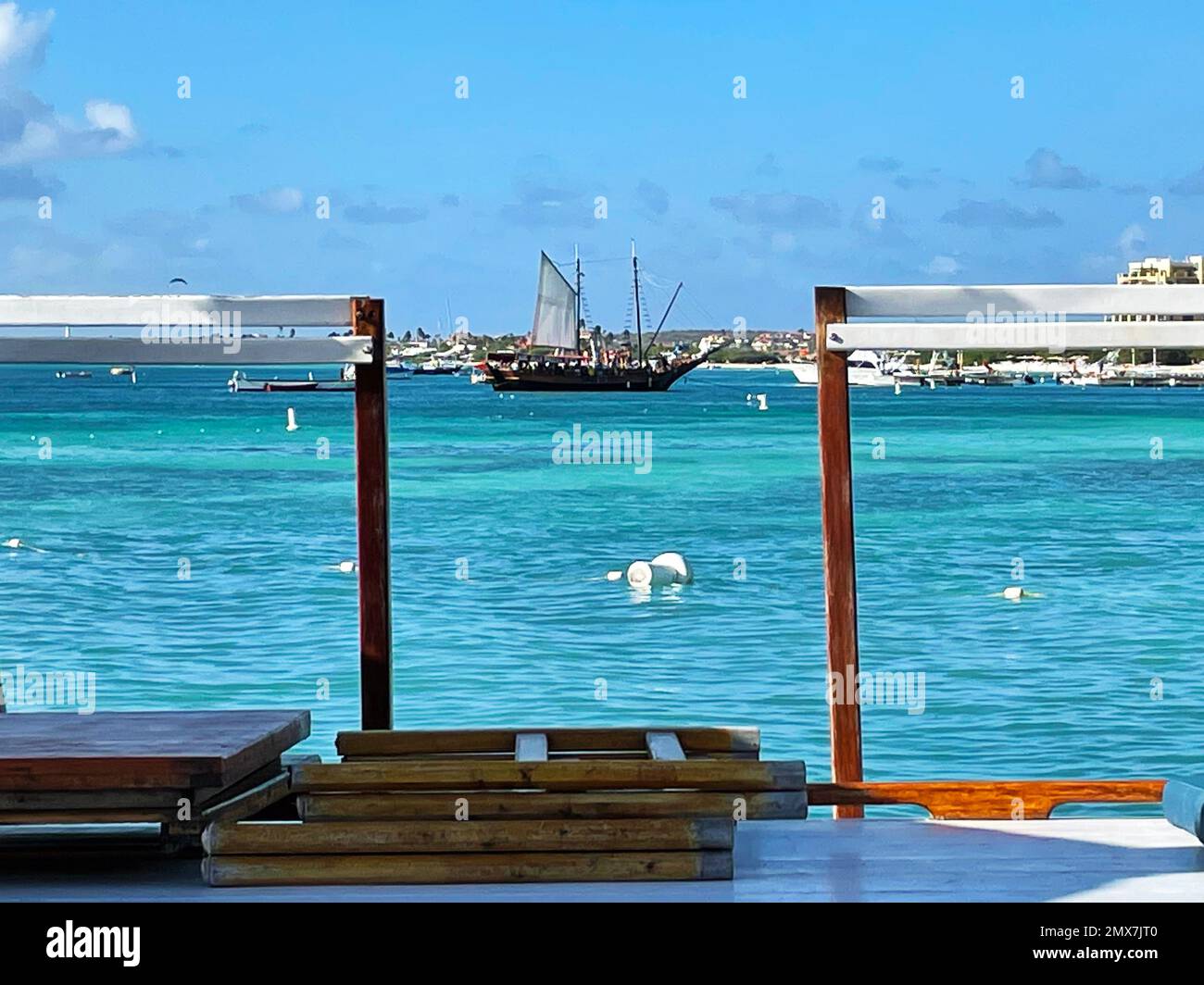 A sailboat framed between the posts of a gangway opening on a pier, Palm Beach, Aruba. Stock Photo