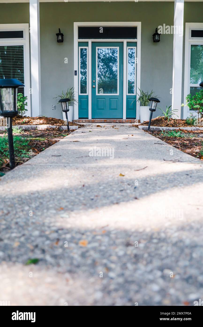 A simple walkway to an Acadia style gray house with a turquoise door with transom windows Stock Photo