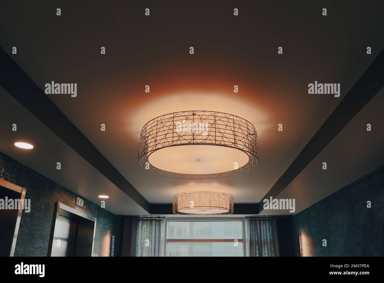 A glowing and lit drum light with black metal accents on a warm ceiling