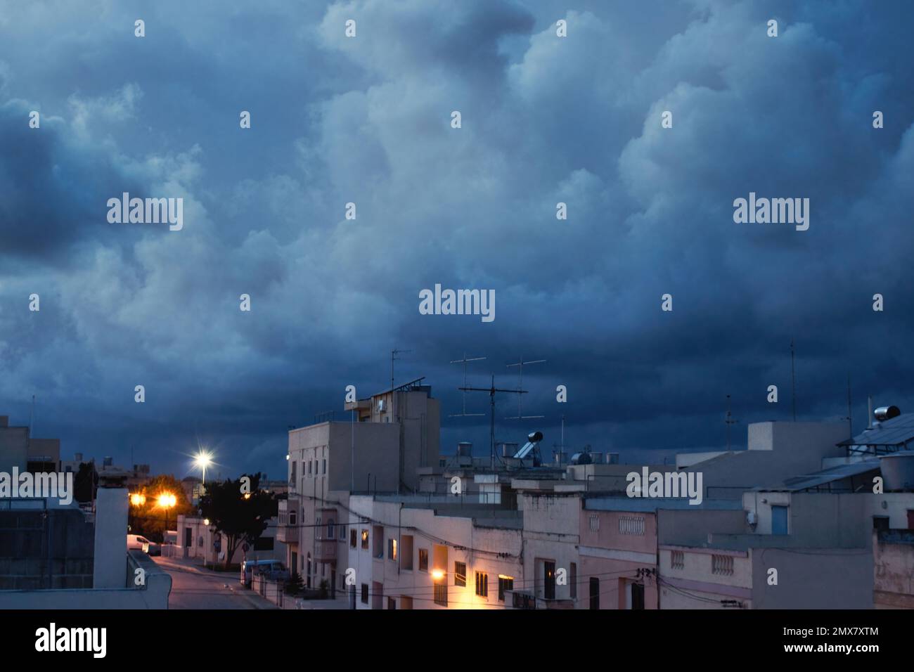 A dark blue overcast sky above a residential street with rows of houses Stock Photo