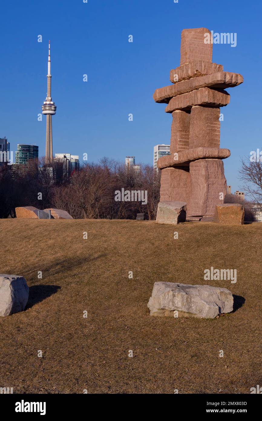 We're looking NE at Toronto Inukshuk Park to the iconic CN Tower near the shores of Lake Ontario, Canada.  The granite Inukshuk is 30 feet tall. Stock Photo