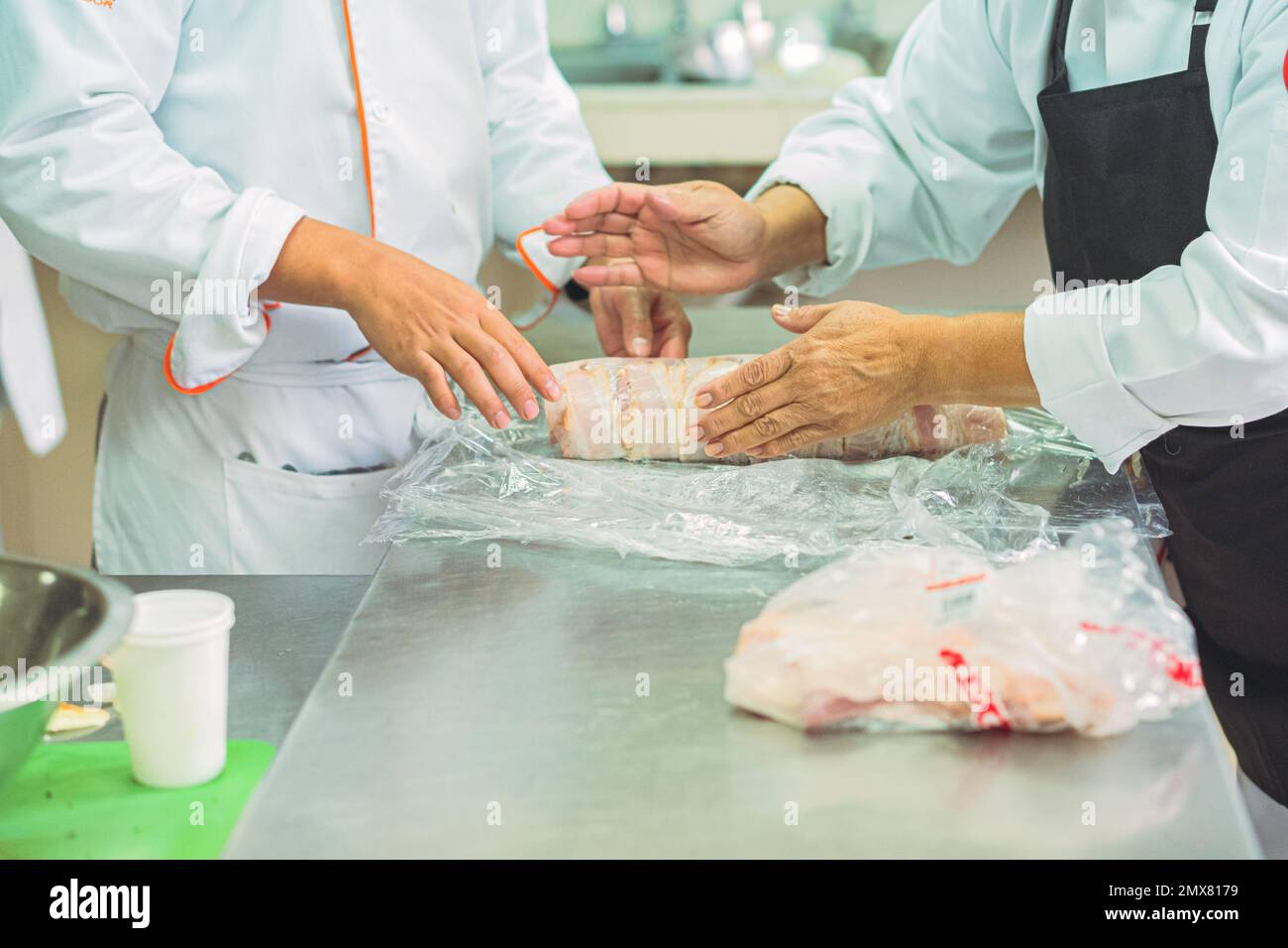 Crop anonymous cooks in uniforms and aprons rolling raw meat in