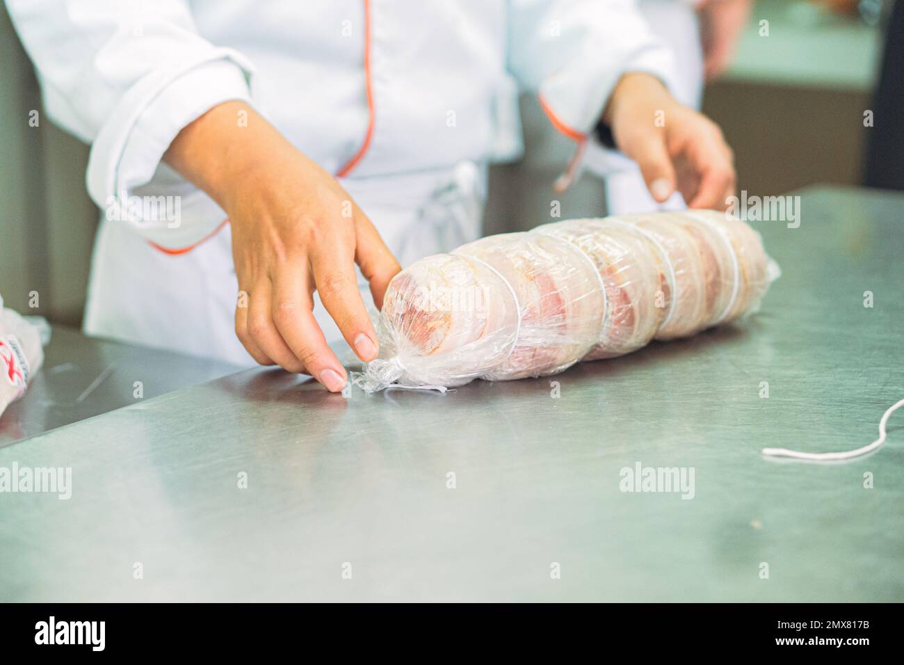 Crop anonymous cooks in uniforms and aprons rolling raw meat in