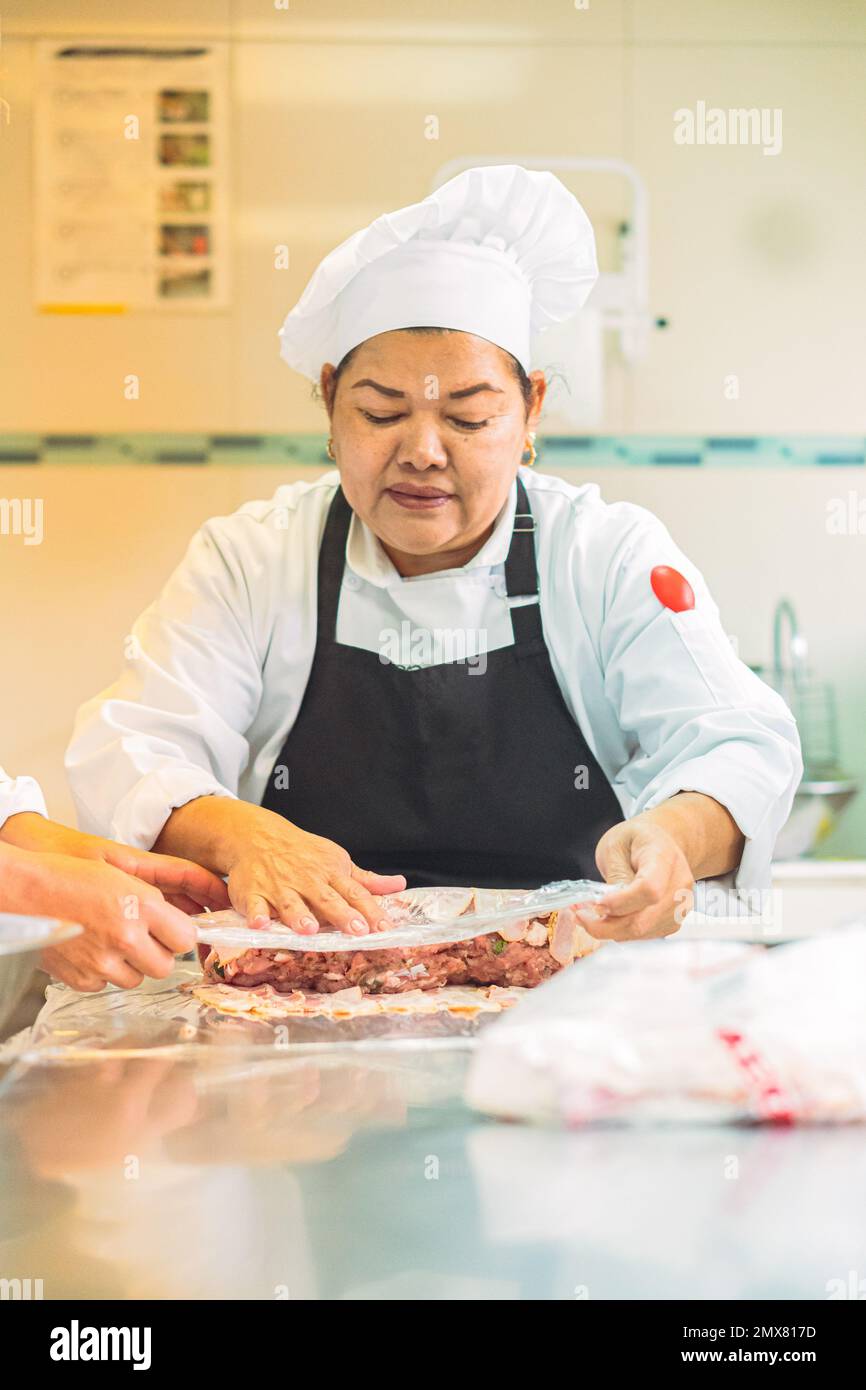 Female chef in uniform and apron covering raw meat with clingfilm while