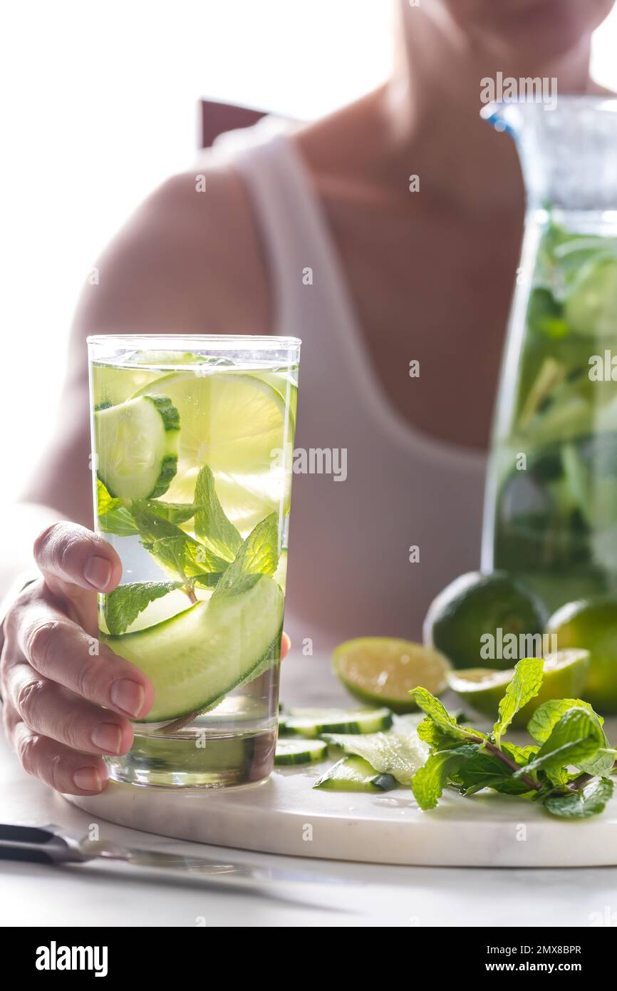A woman holding a tall glass of cucumber infused water with ingredients beside. Stock Photo