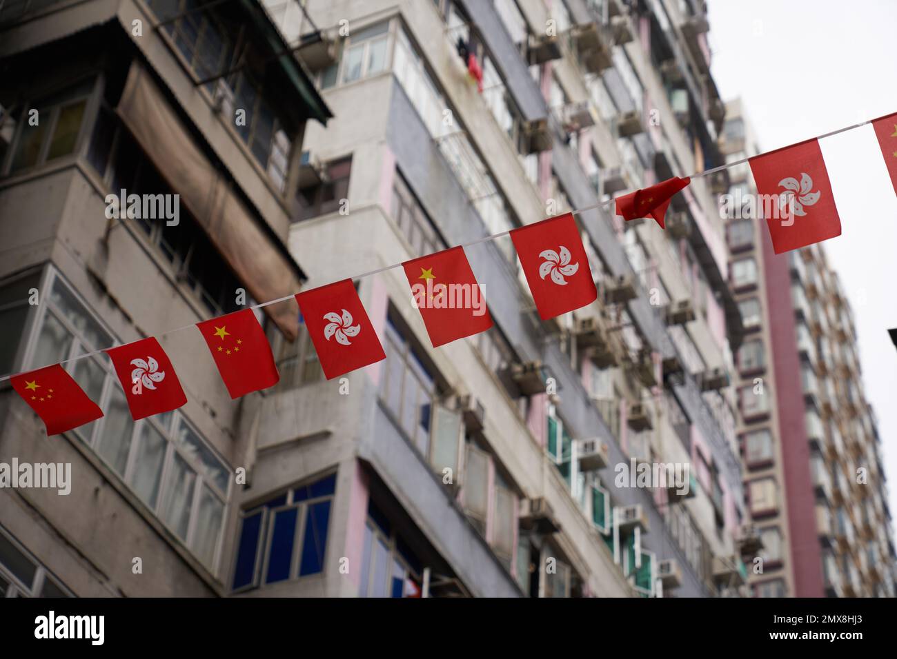 A row of Chinese and Hong Kong flags hang over an urban street in central Hong Kong with apartment buildings in the background. Stock Photo