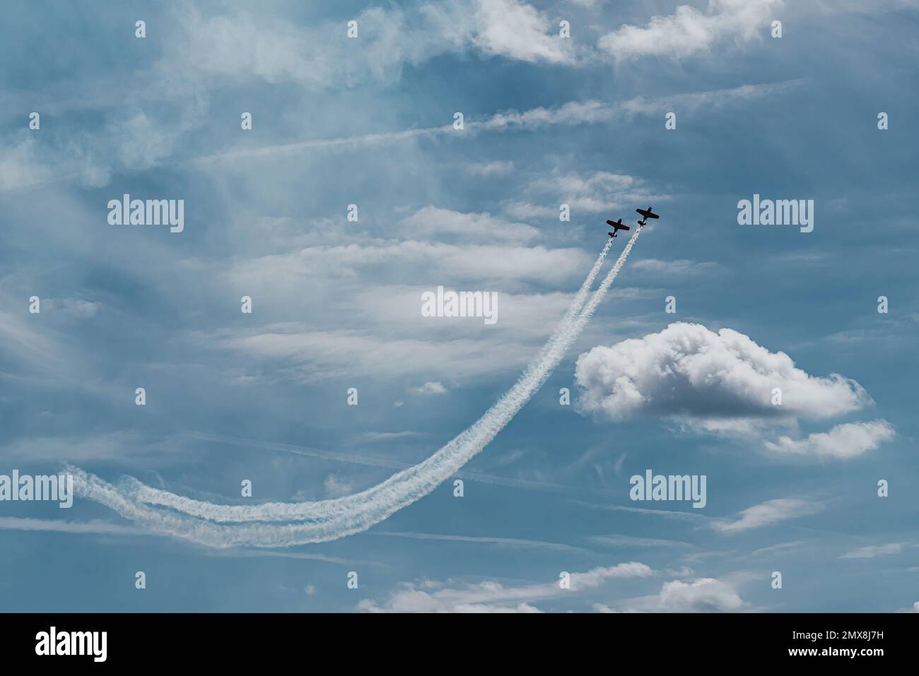 two small planes fly parallel in upward trajectory near a cloud over blue sky. condensation trails and clouds. concept of friendship and loyalty. Mutu Stock Photo