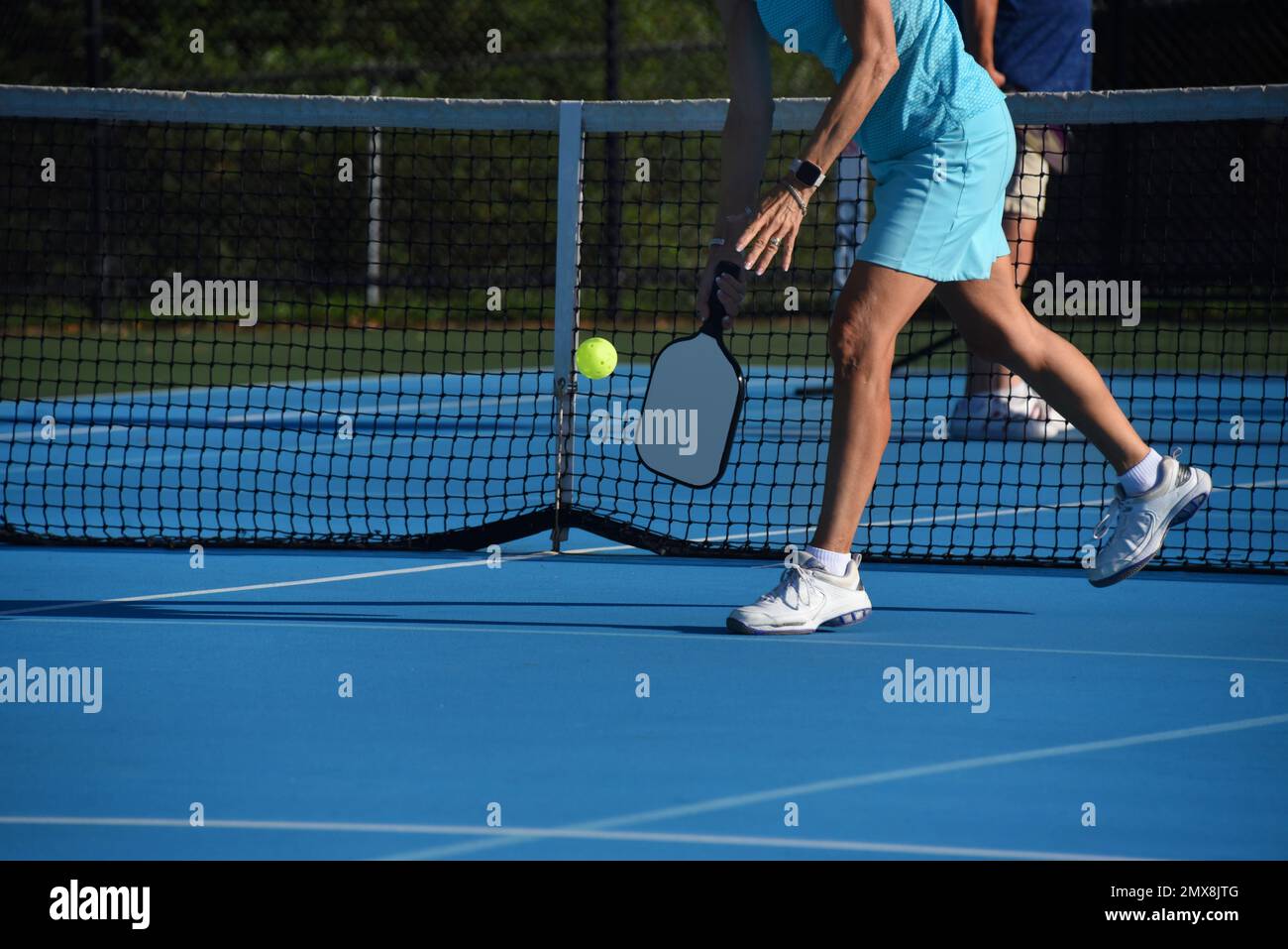 Senior female leans down to serve the ball during a pickle ball match in Asheville, North Carolina. Stock Photo