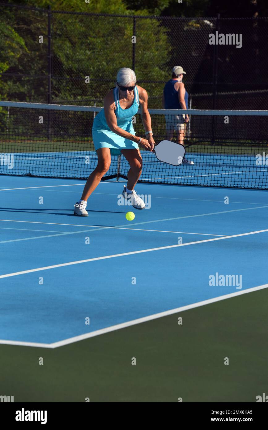 Senior female reaches to return a pickle ball during a game in Asheville, North Carolina.  She is wearing a turquoise tennis outfit. Stock Photo