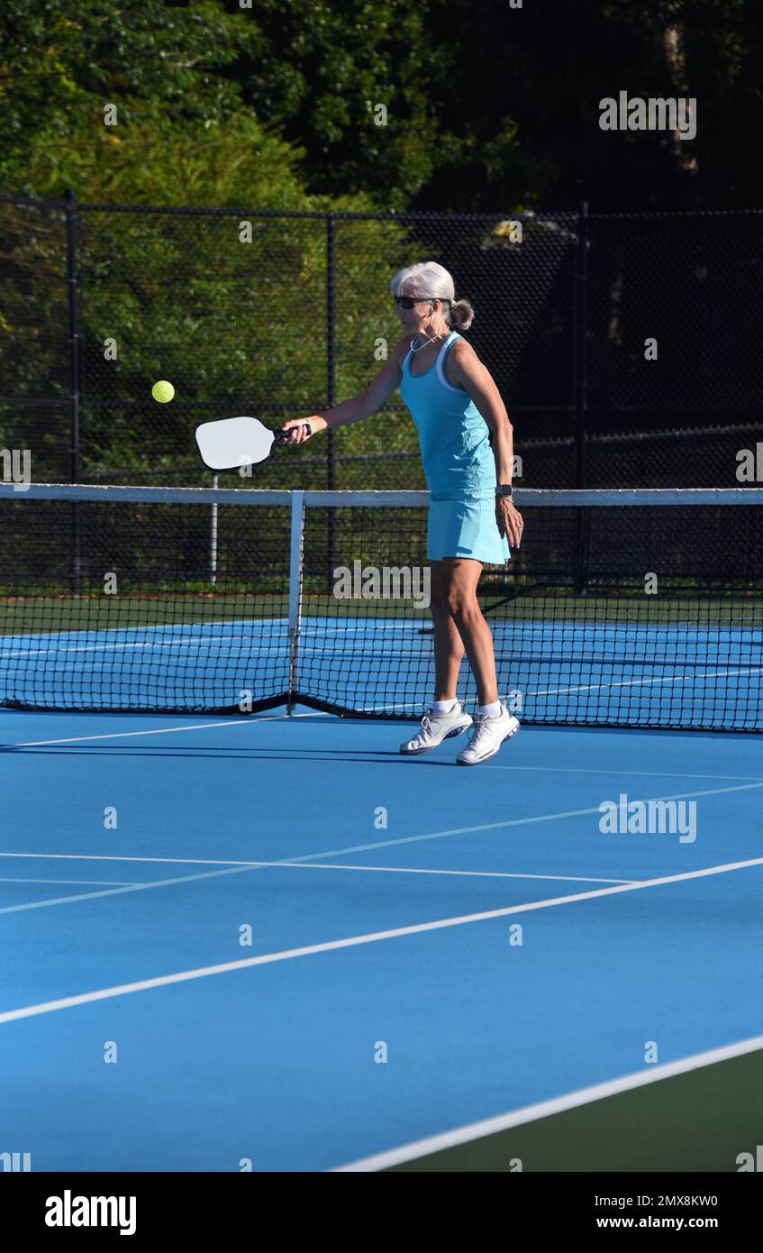 Senior female returns the pickle ball during a match in Asheville, North Carolina.  She is wearing a turquoise tennis skirt and top. Stock Photo