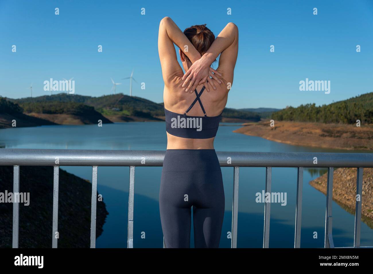 Rear view of a sporty woman doing an arm stretch warm up exercise, outside by a lake. Stock Photo