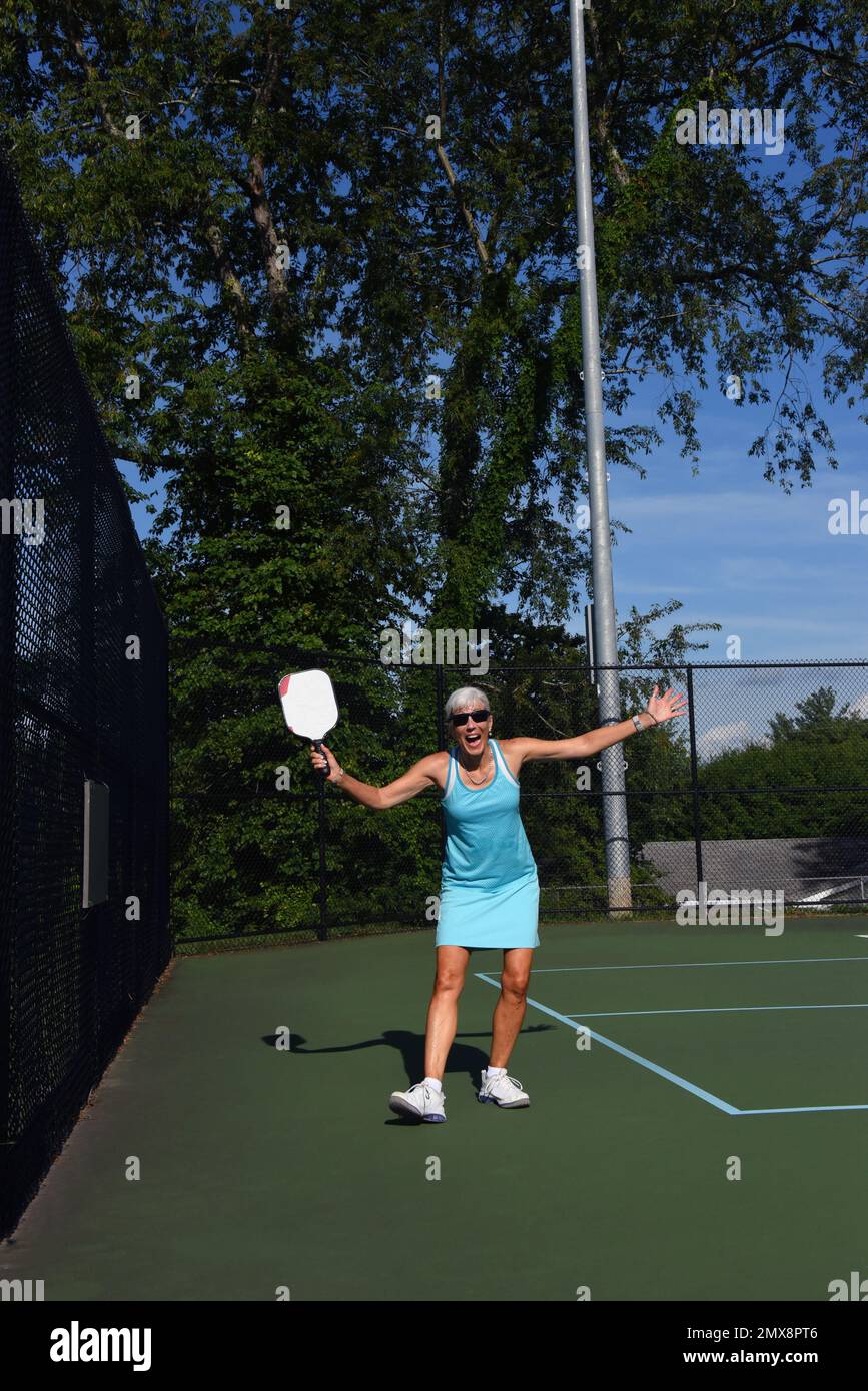 Senior female poses holding her pickle ball paddle.  She is smiling and filled with enthusiasm for the game. Stock Photo