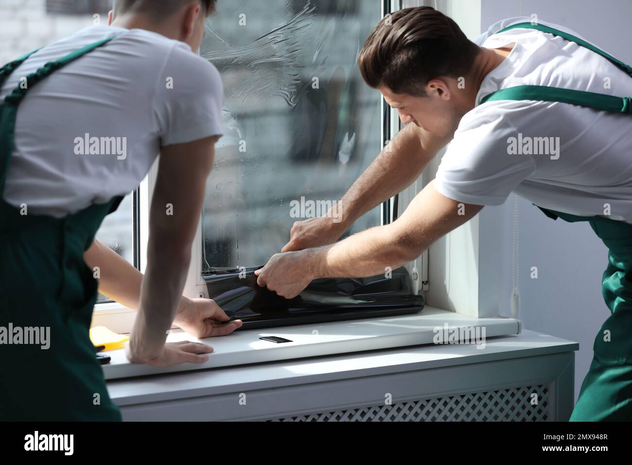 Professional workers tinting window with foil indoors Stock Photo