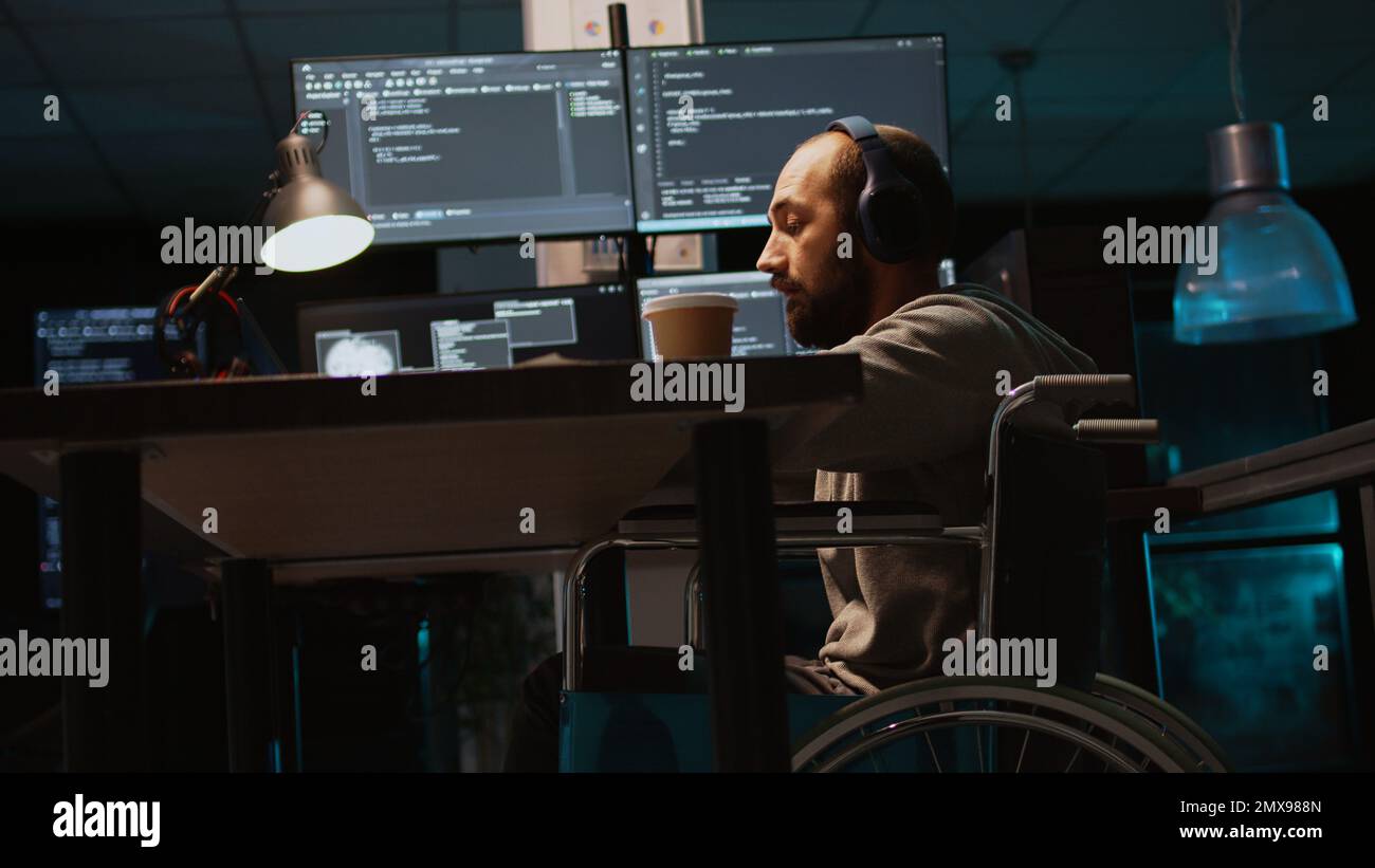 Young engineer with chronic disability working on IT software coding, using source code and data. Male coder wheelchair user with impairment developing system interface. Handheld shot. Stock Photo