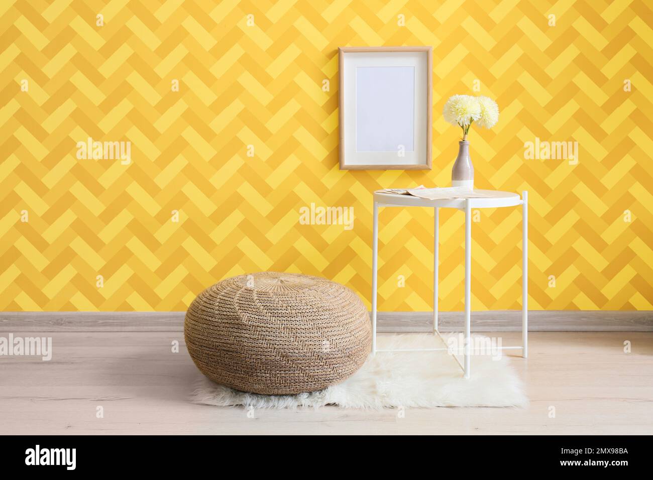 Table with flowers in vase and pouf near yellow wall in room Stock Photo