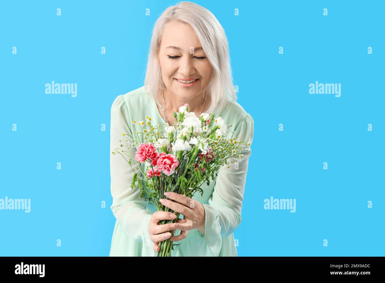Beautiful mature woman with bouquet of flowers on light blue background ...