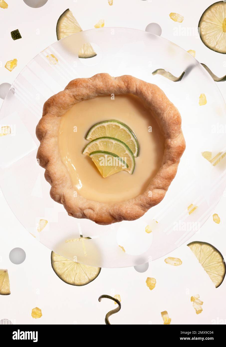 Lime tart of tartlet on decorative glass plate.  Overhead photograph, plate is surrounded by lime twists, lime slices and lime rock candy. Stock Photo
