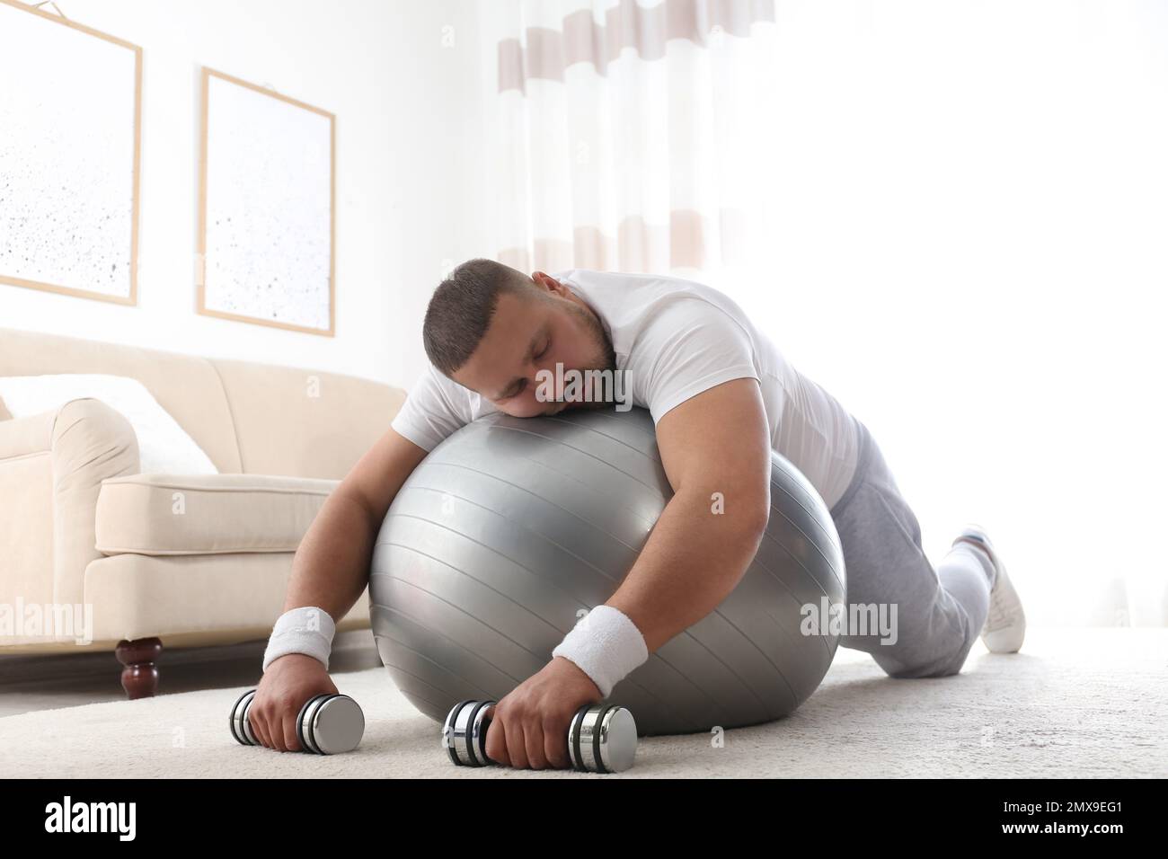 Lazy overweight man with sport equipment sleeping on floor at home Stock Photo