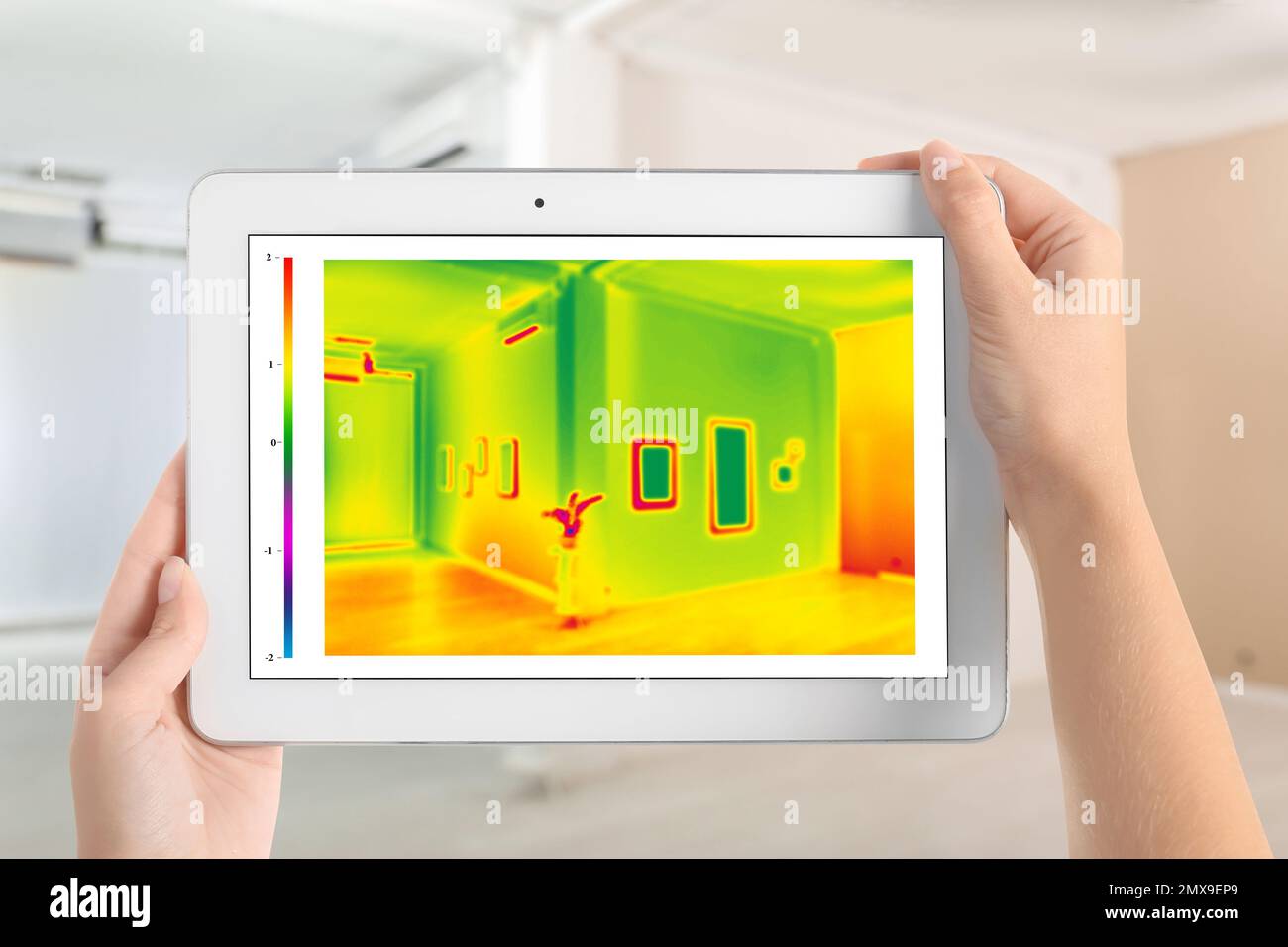 Woman detecting heat loss in room using thermal viewer on tablet