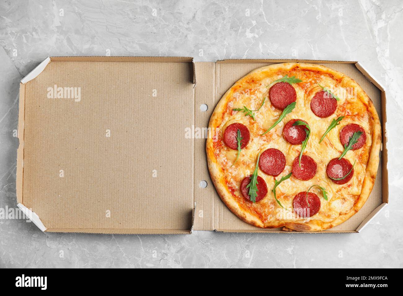 Tasty pepperoni pizza in cardboard box on light grey marble table, top