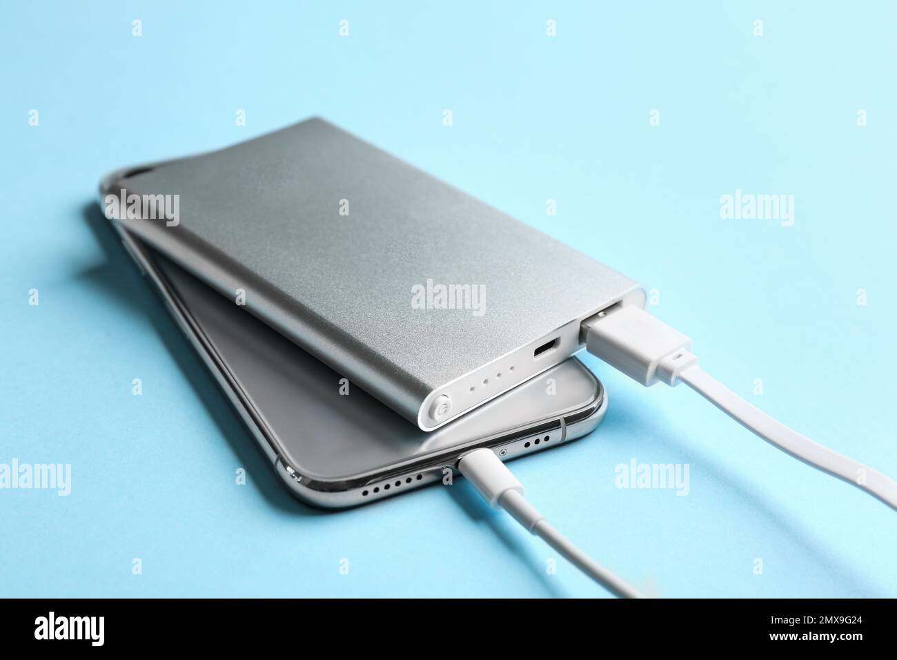 Mobile phone charging with power bank on light blue background, closeup