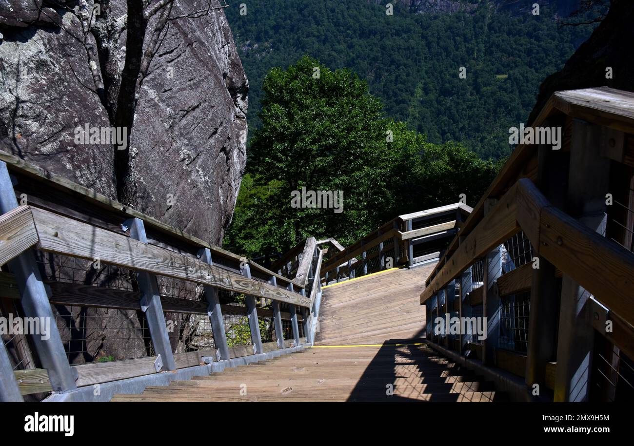Steep steps ascend to the top of Chimney Rock, Chimney Rock State Park, North Carolina.  Stairs are wooden with metal and wood rails.  Rock bluff is b Stock Photo