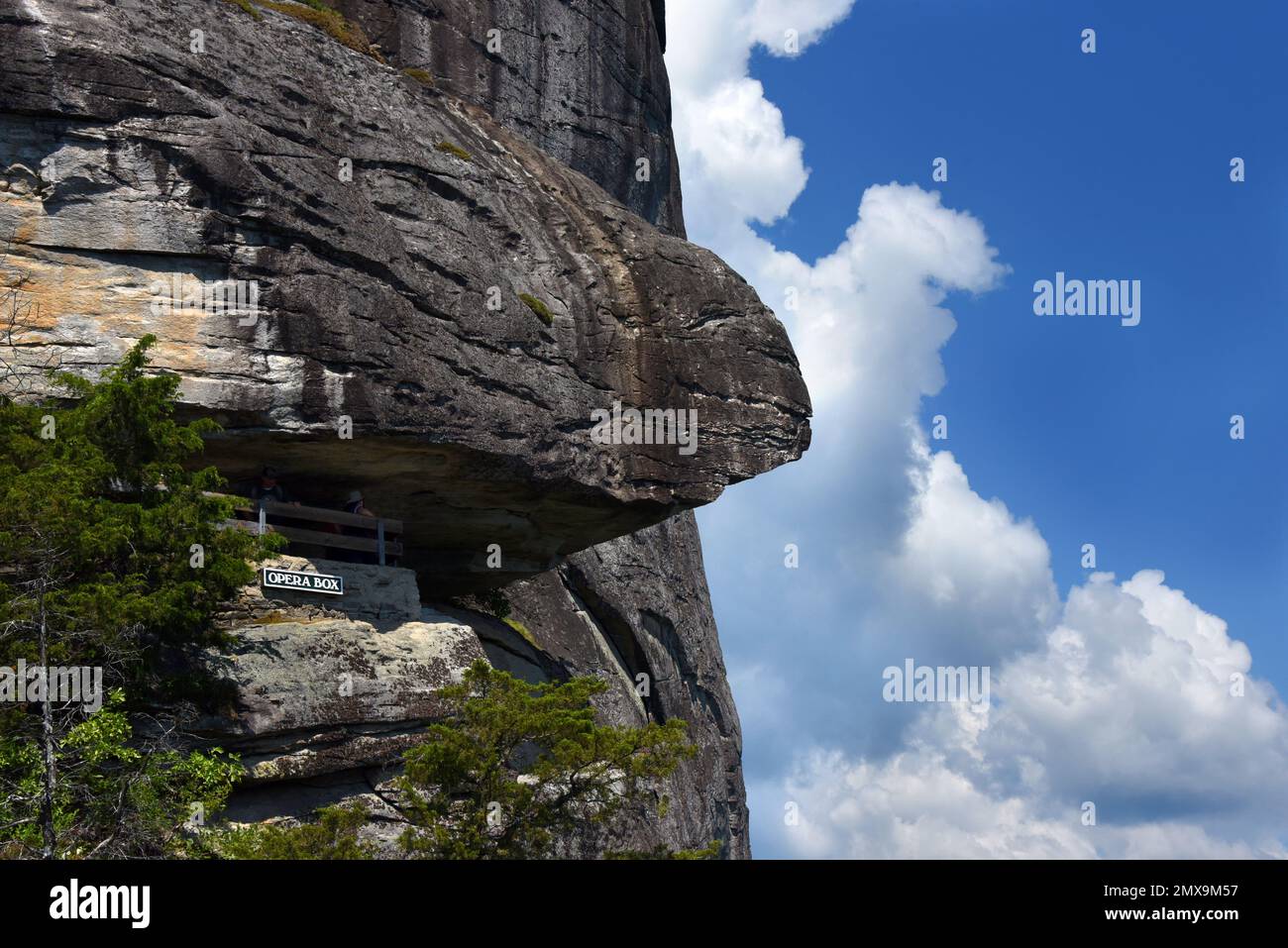 Visitors pause at the Opera Box view point, at Chimney Rock State Park, North Carolina.  Rocky bluff hangs over trail. Stock Photo