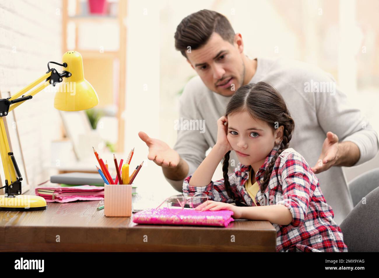 Father scolding his daughter while helping with homework at table ...