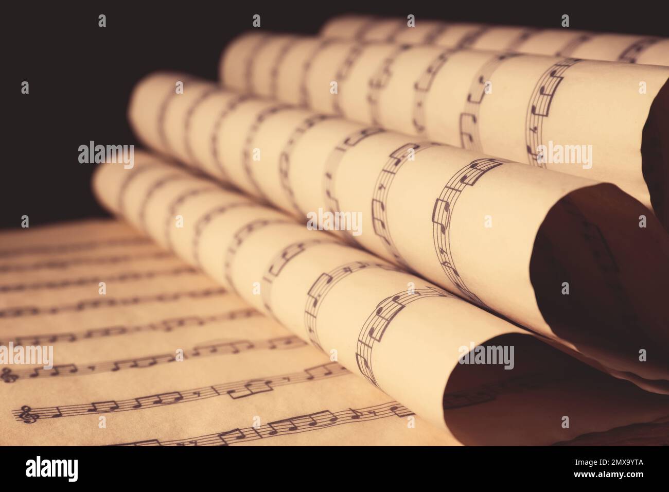 Old wrapped sheets with music notes on black background, closeup Stock