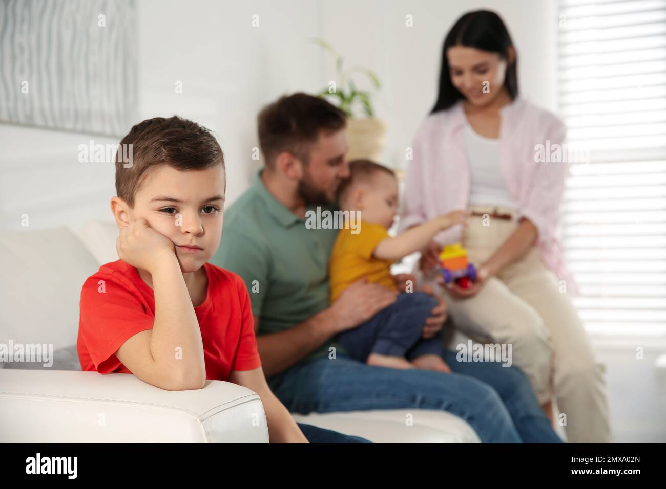 Unhappy little boy feeling jealous while parents spending time with his  baby brother at home Stock Photo - Alamy