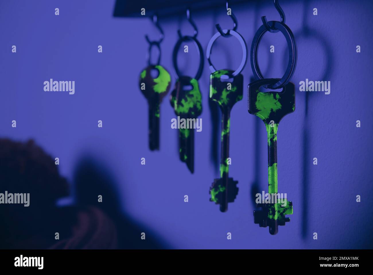 Holder with different keys on wall, view under UV light. Sanitizing objects during coronavirus outbreak Stock Photo