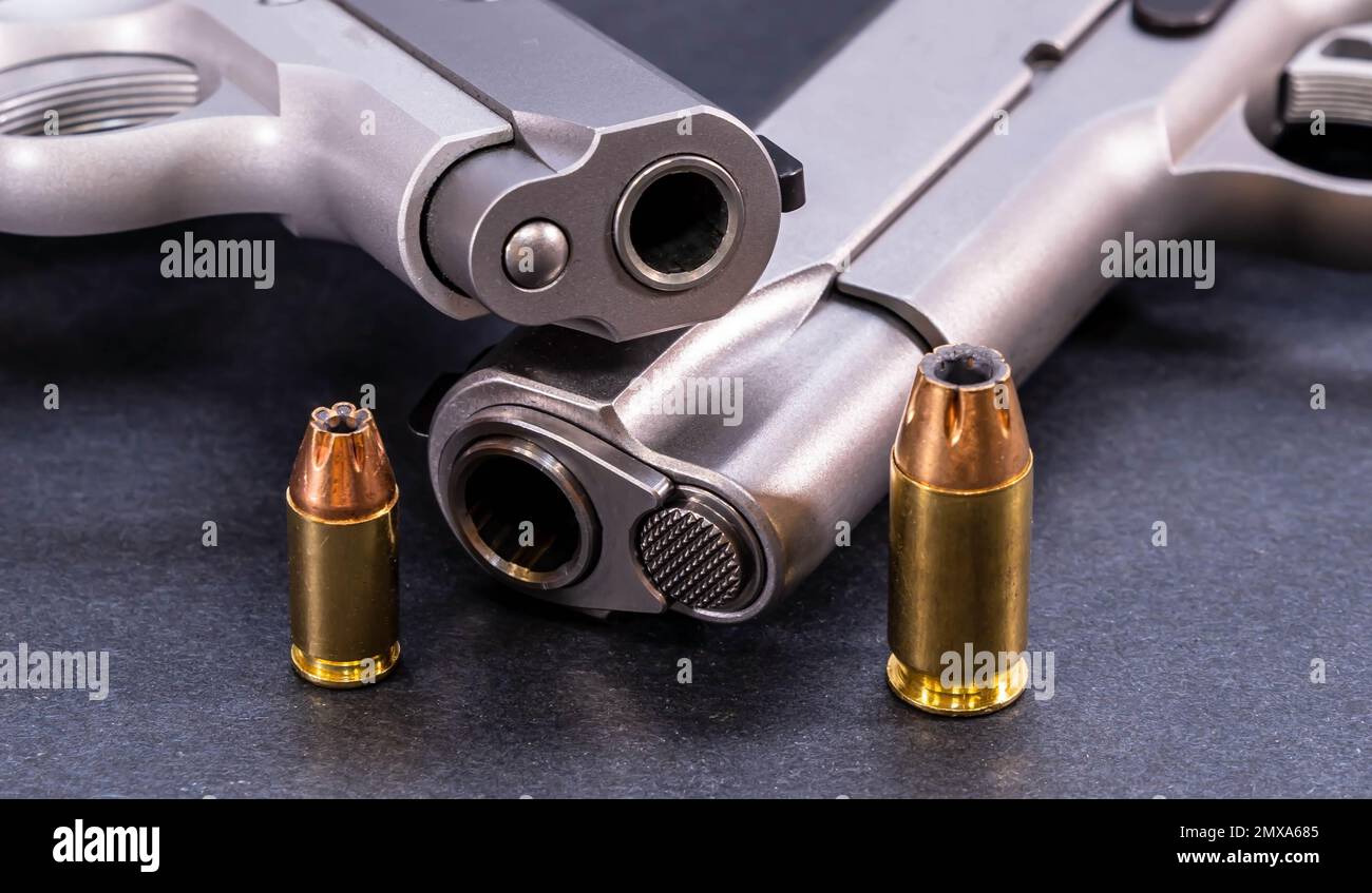 Two stainless steel 1911 pistols, one a 45 ACP and the other a 380 caliber with a hollow point bullet for each next to it on a black background Stock Photo