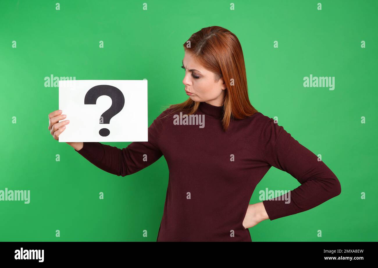 Confused woman holding question mark sign on green background Stock ...