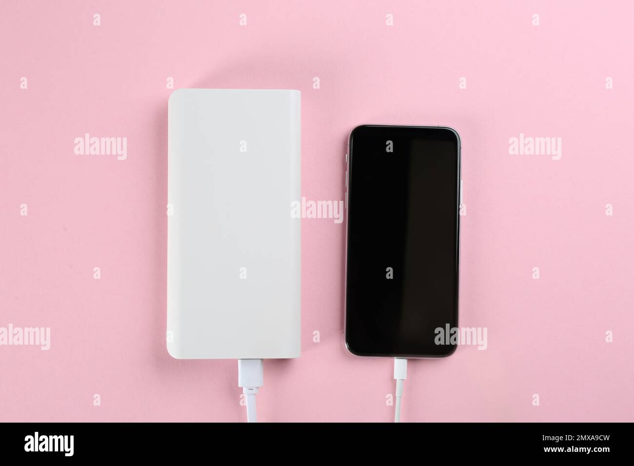 Mobile phone charging with power bank on pink background, flat lay