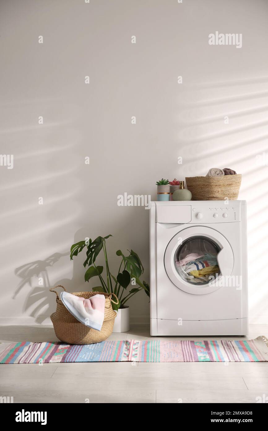 Modern washing machine and wicker basket with laundry near white wall ...