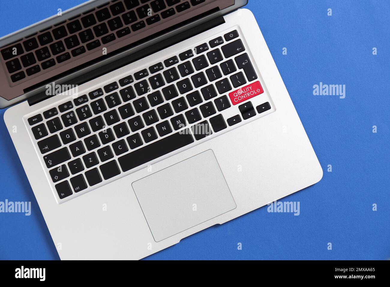 Modern laptop with quality control button on blue background, top view