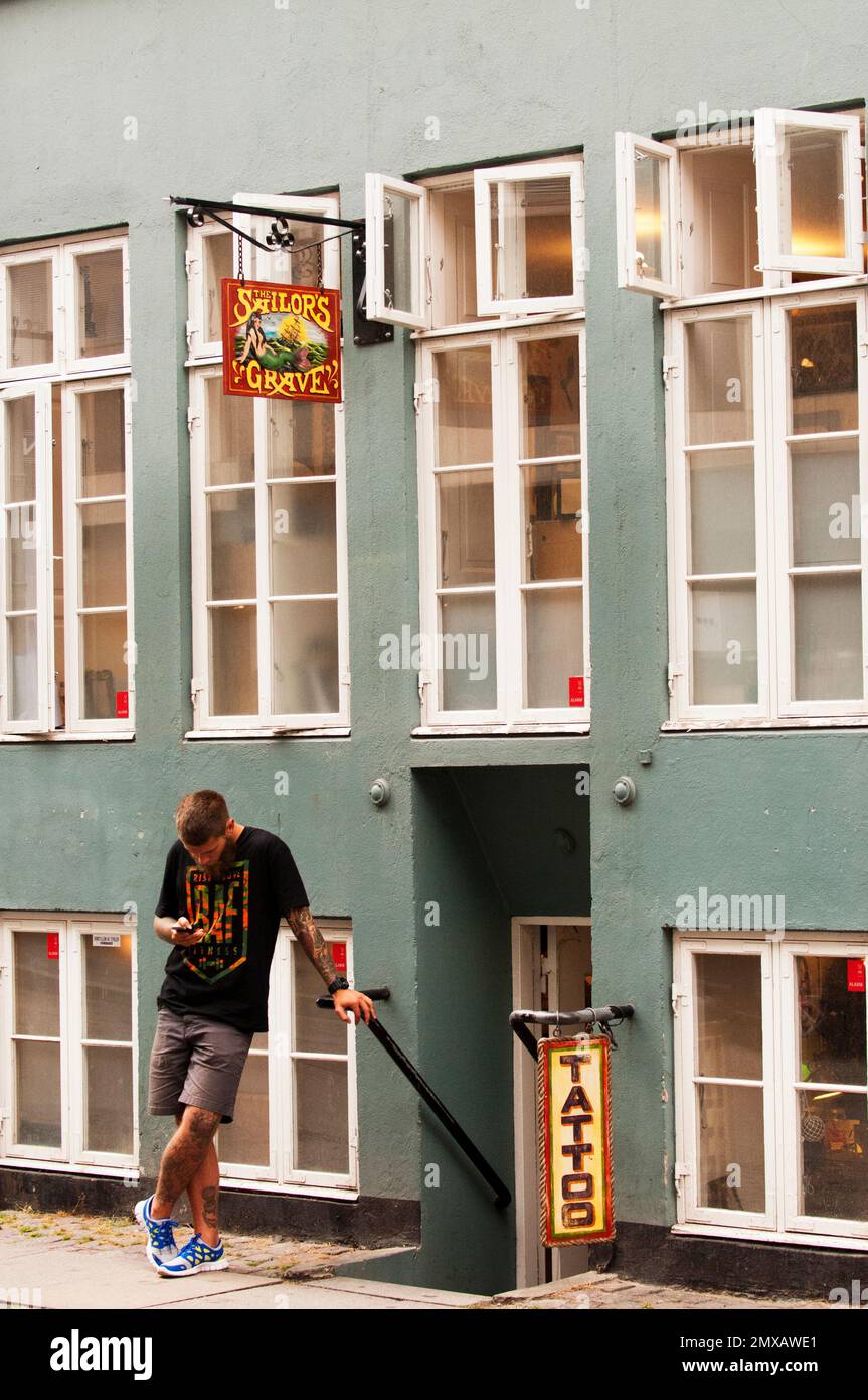 Young man checks his phone outside a tattoo parlour. Stock Photo