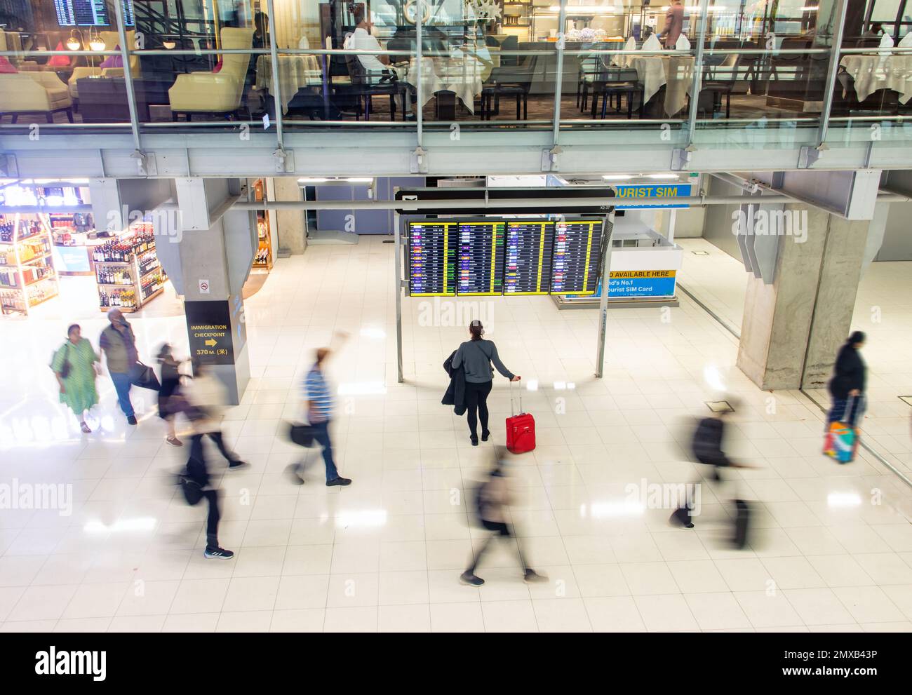 Blurred people walking in an airport hall next to a standing woman reading information from the departure board Stock Photo