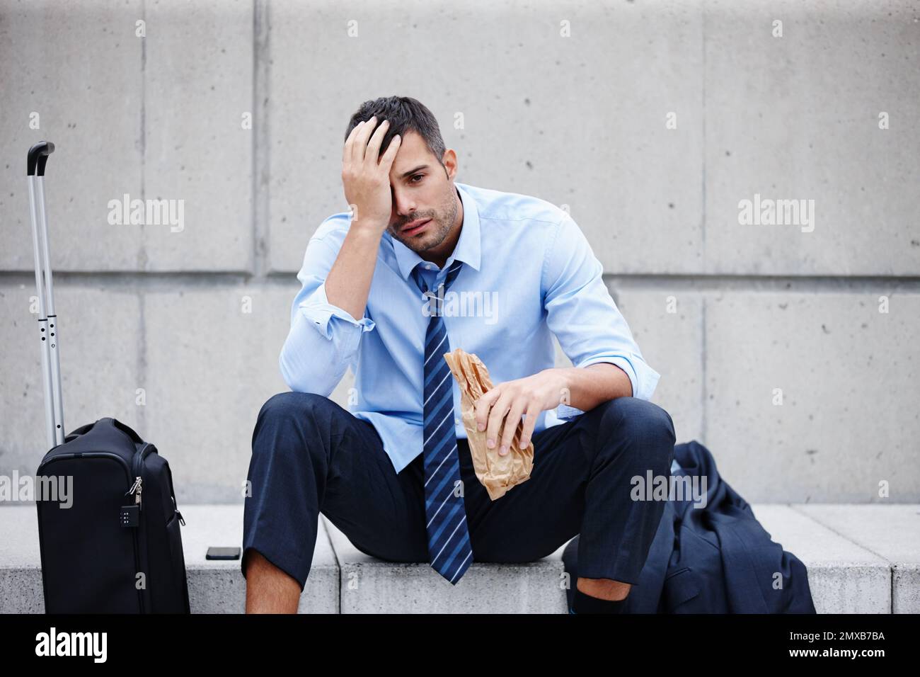 Down on his luck. A young businessman sitting outdoors and drinking while looking dejected. Stock Photo