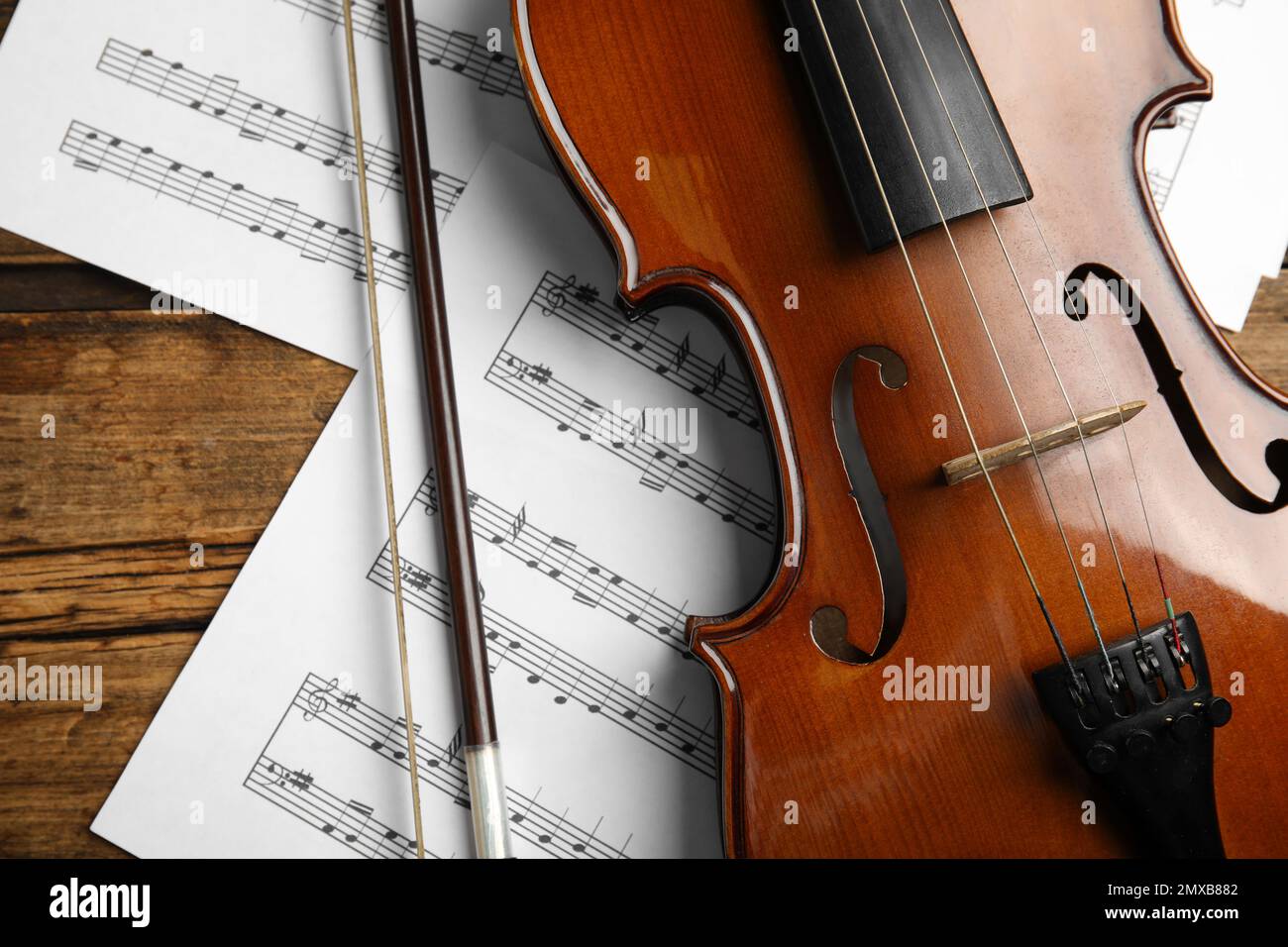 Beautiful violin, bow and note sheets on wooden table, flat lay Stock Photo