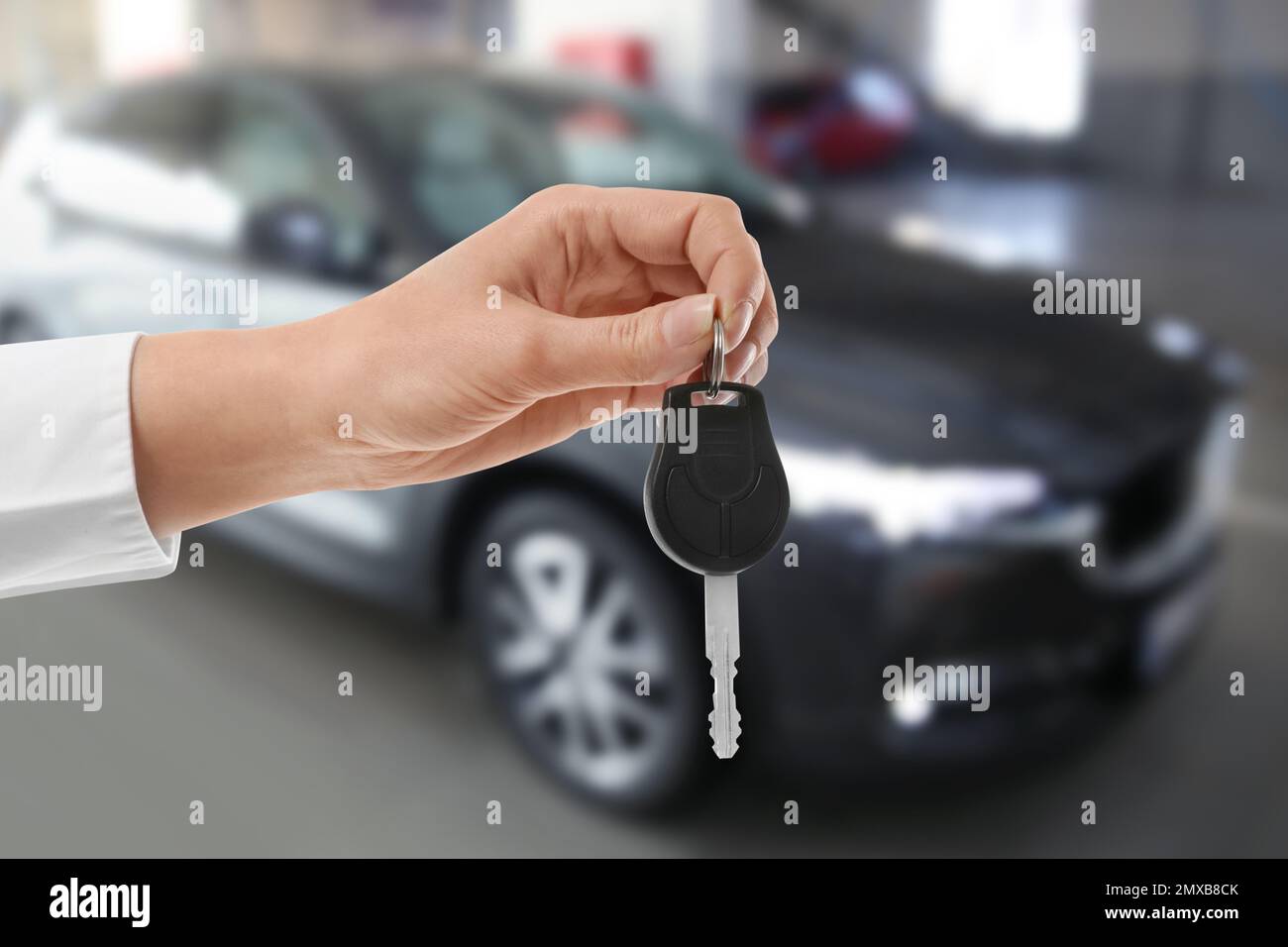 Woman with key near new automobile indoors, closeup Stock Photo