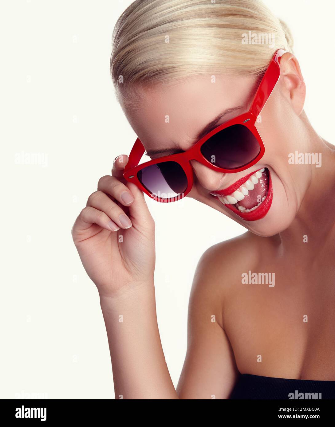 Blonde bombshell. A smiling blonde wearing red sunglasses against an isolated background. Stock Photo
